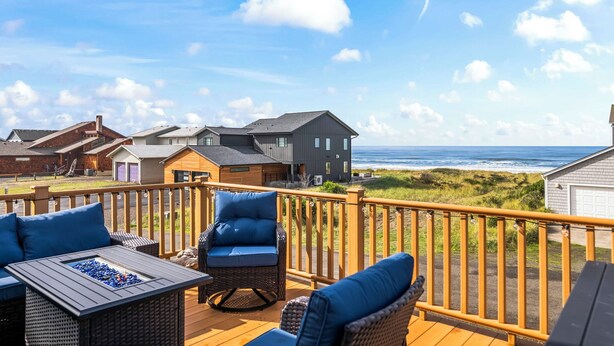 A deck with outdoor seating, a fire pit, and a view of the ocean and beach houses. - Beachfront ADA Cottage: Elevator, Sauna, fire pit (Westport)