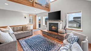 A spacious living room with a fireplace, a large TV, and a balcony. - Beachfront ADA Cottage: Elevator, Sauna, fire pit (Westport)