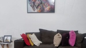 Una sala de estar con un sofá seccional marrón oscuro, un cuadro abstracto enmarcado y una mesita con un marco de fotos.