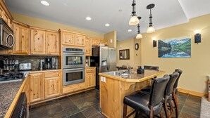 A kitchen with wooden cabinets, stainless steel appliances, a granite countertop, and a bar area with stools.