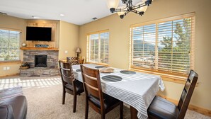 A dining area with a stone fireplace, a flat-screen TV, and large windows.