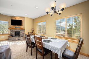 A dining area with a stone fireplace, a flat-screen TV, and large windows.