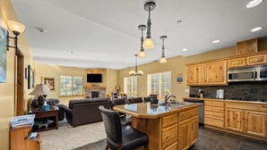A modern kitchen with a central island, wooden cabinets, and a stone backsplash.