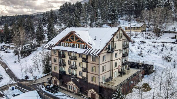 A multi-story hotel with a snow-covered roof, balconies, and a ski slope in the background.