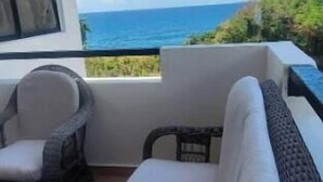 Un balcon avec un canapé et des fauteuils, offrant une vue panoramique sur l’océan.