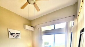 Une chambre à coucher avec un lit, un ventilateur de plafond, une fenêtre et un téléviseur.