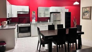 Une cuisine de taille réduite avec des murs rouges, des meubles blancs et un coin repas avec des chaises noires.