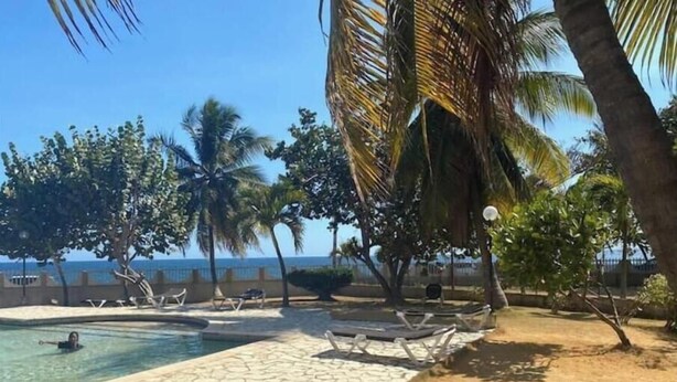 A pool area with lounge chairs and palm trees, overlooking a body of water. - Lovely space to relax (Santo Domingo)