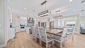 A modern kitchen with white cabinetry, a large island, stainless steel appliances, and a dining area with a wooden table and chairs.