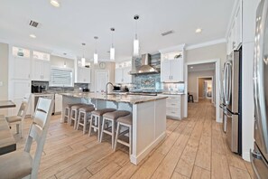 A spacious kitchen with a central island, white cabinetry, stainless steel appliances, and pendant lighting.