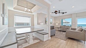 A spacious living area with a kitchen island, ceiling fans, large windows, and a view of the ocean.