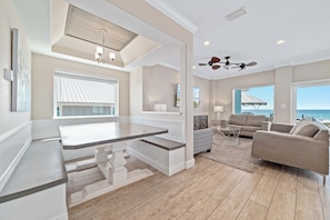 A spacious living area with a kitchen island, ceiling fans, large windows, and a view of the ocean.