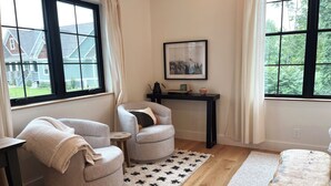 A cozy room with two armchairs, a small table, a wooden bench, and a rug with a black and white pattern. - Allora (Hendersonville)