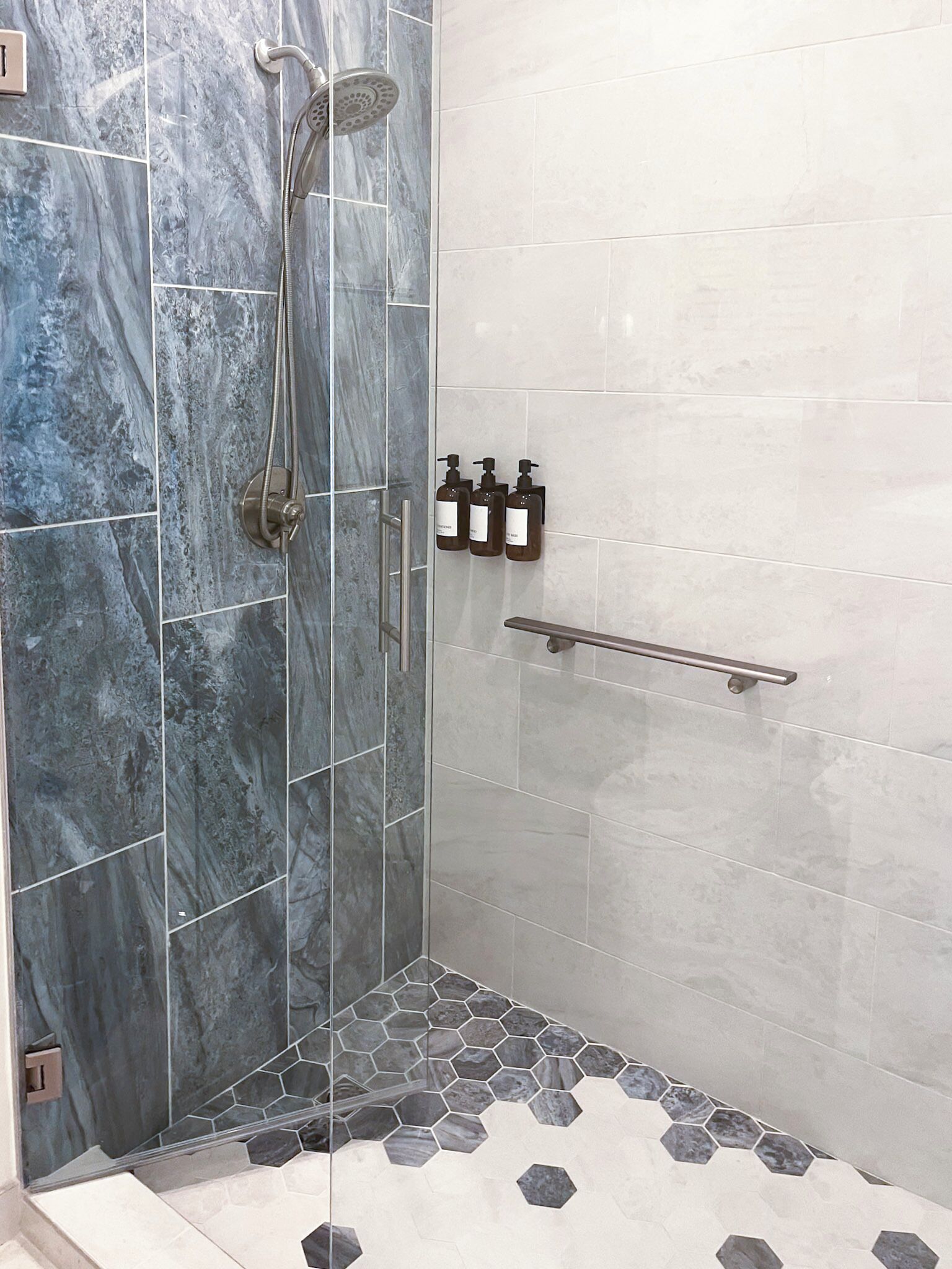 Dusche mit Glastür, Handbrause und drei Seifenspendern an der Wand.
