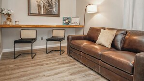 Un salon avec un canapé en cuir marron, deux fauteuils en osier, une table basse en bois, une œuvre d’art encadrée, un disque vinyle et une lampe sur pied.