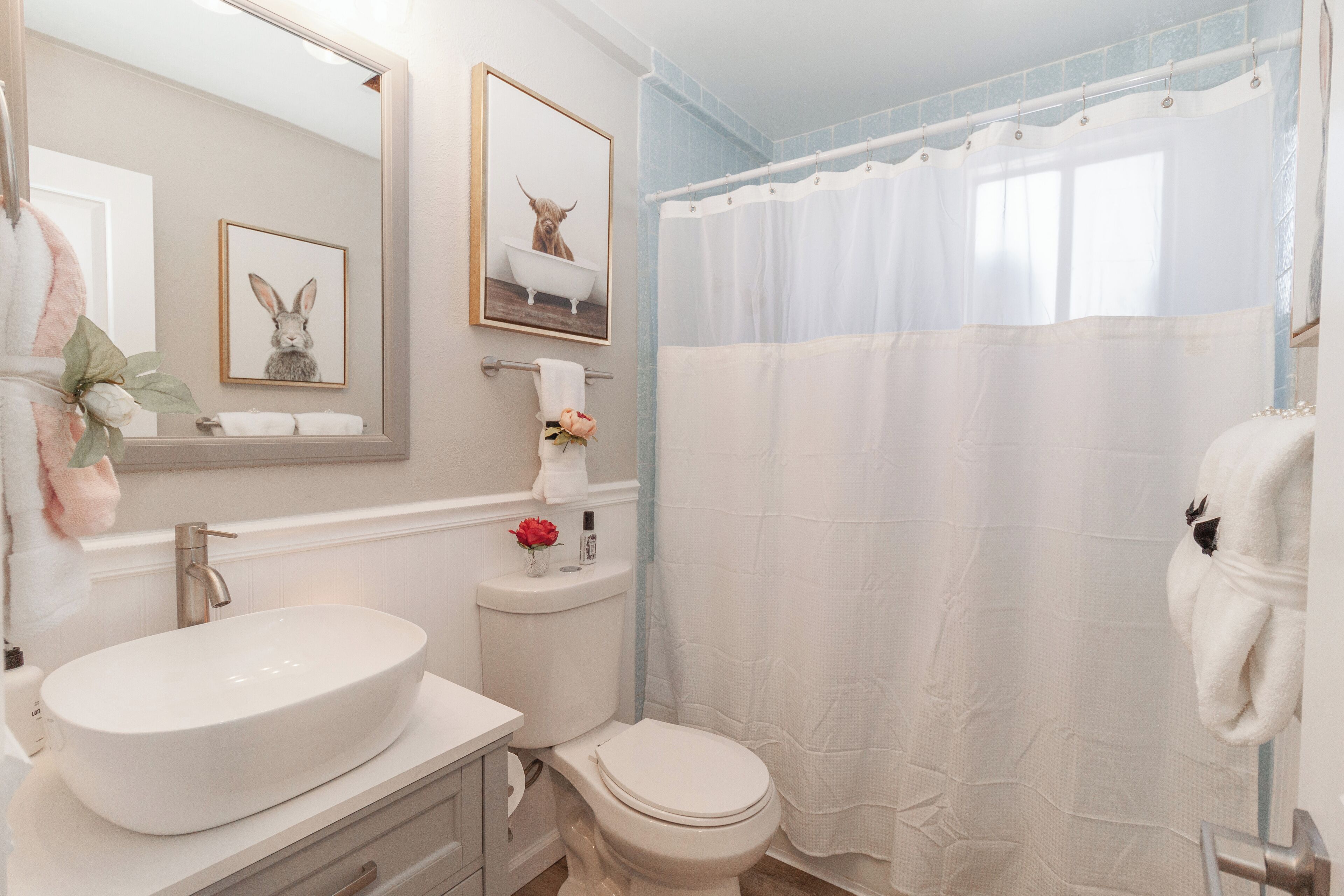 A bathroom with a white sink, toilet, and shower curtain. There are framed pictures on the wall and a towel rack with towels.