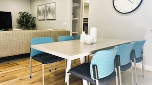 Una sala de estar moderna con una mesa de comedor de madera, sillas azules, un sofá, un televisor y arte abstracto en la pared.