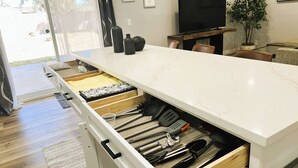 Una cocina con encimera de mármol blanco, un cajón empotrado con utensilios, un televisor y una planta en maceta.