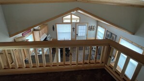 A loft-style room with a sloped ceiling, wooden beams, and a balcony railing. - Cozy Cabin w/ loft in charming Colorado Springs near USAFA (Colorado Springs)