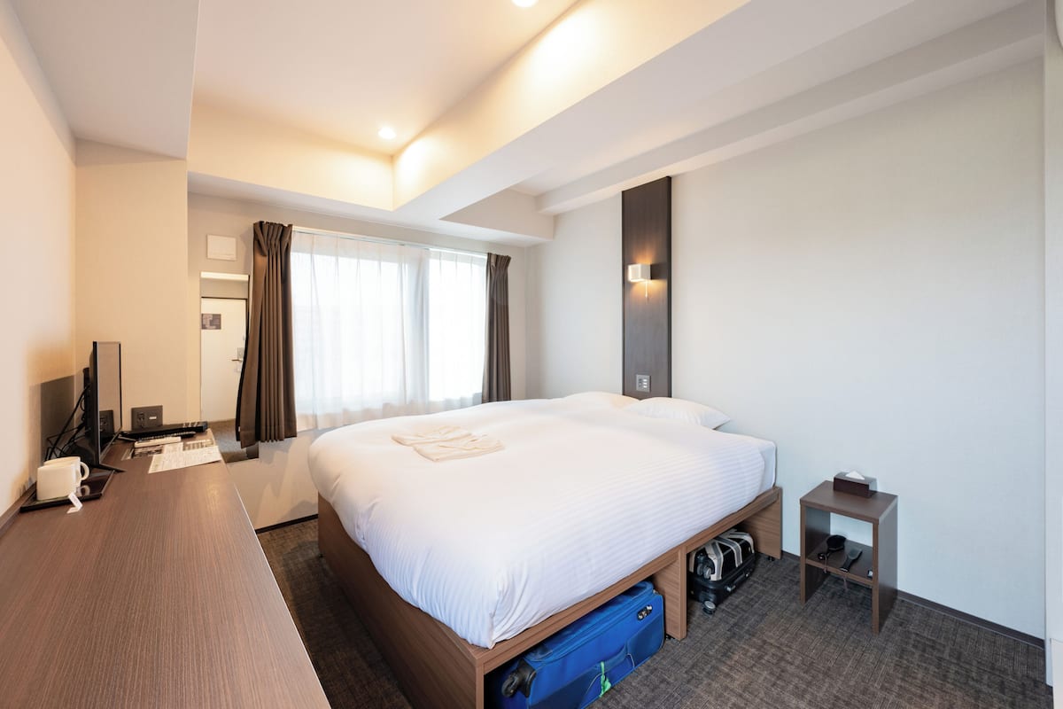 A hotel room with a large bed, a desk, a chair, a TV, and a window with curtains.