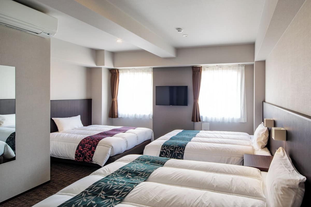 A hotel room with three beds, a flat-screen TV, and a large window with curtains.