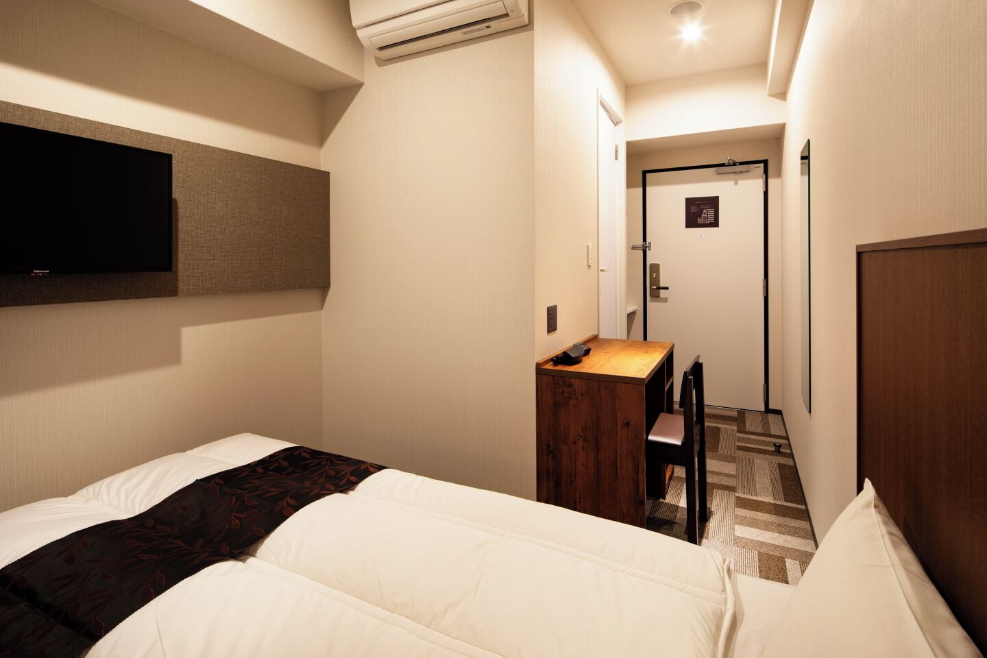 Una habitació d'hotel amb un llit, un escriptori i una televisió penjada a la paret.
