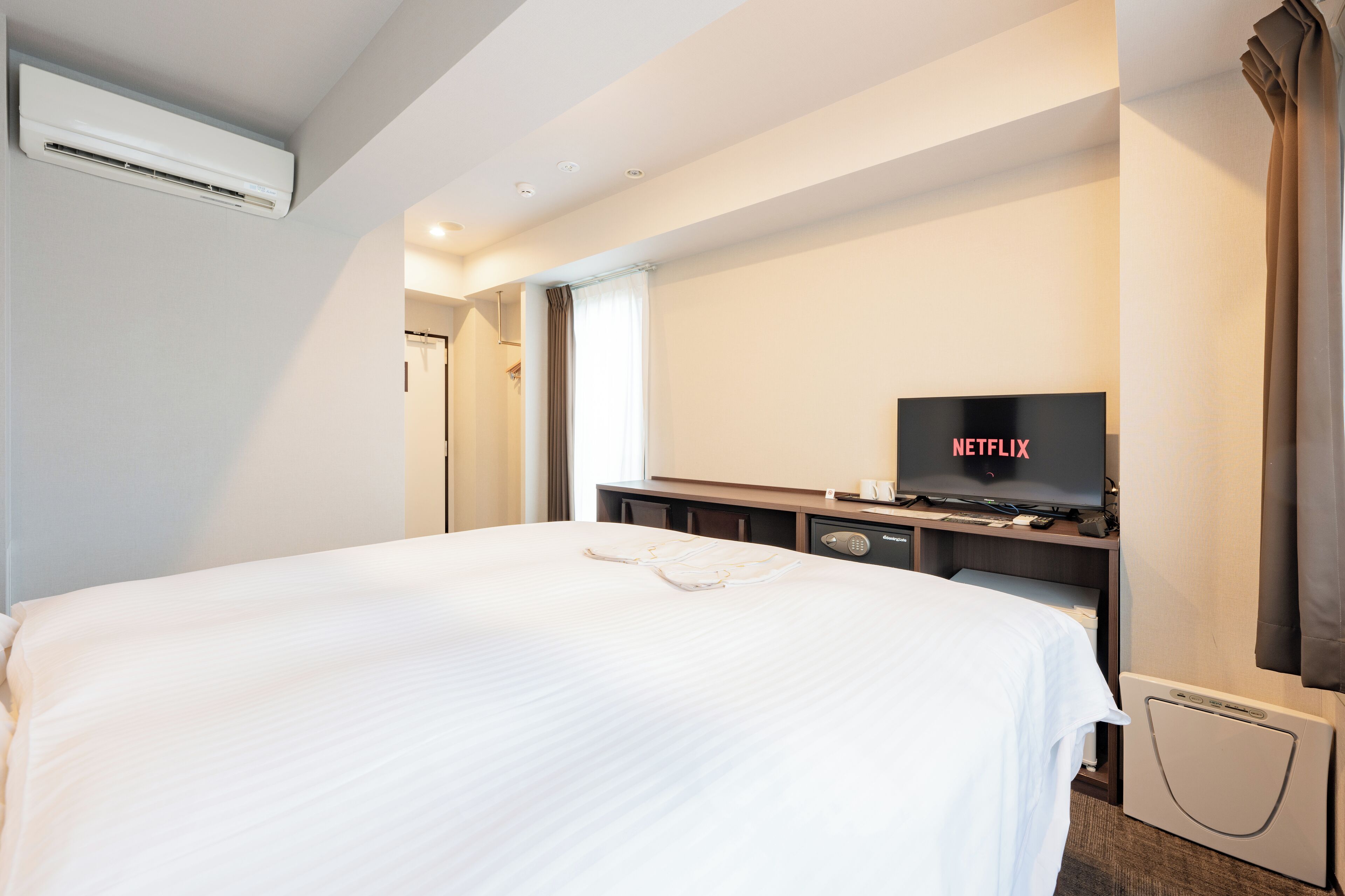 Ein Hotelzimmer mit einem großen Bett, einem Fernseher, der 'NETFLIX' anzeigt, und einer Wandklimaanlage.