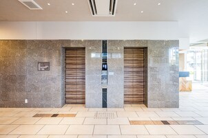 A modern lobby with marble walls, two elevators, and a tiled floor.