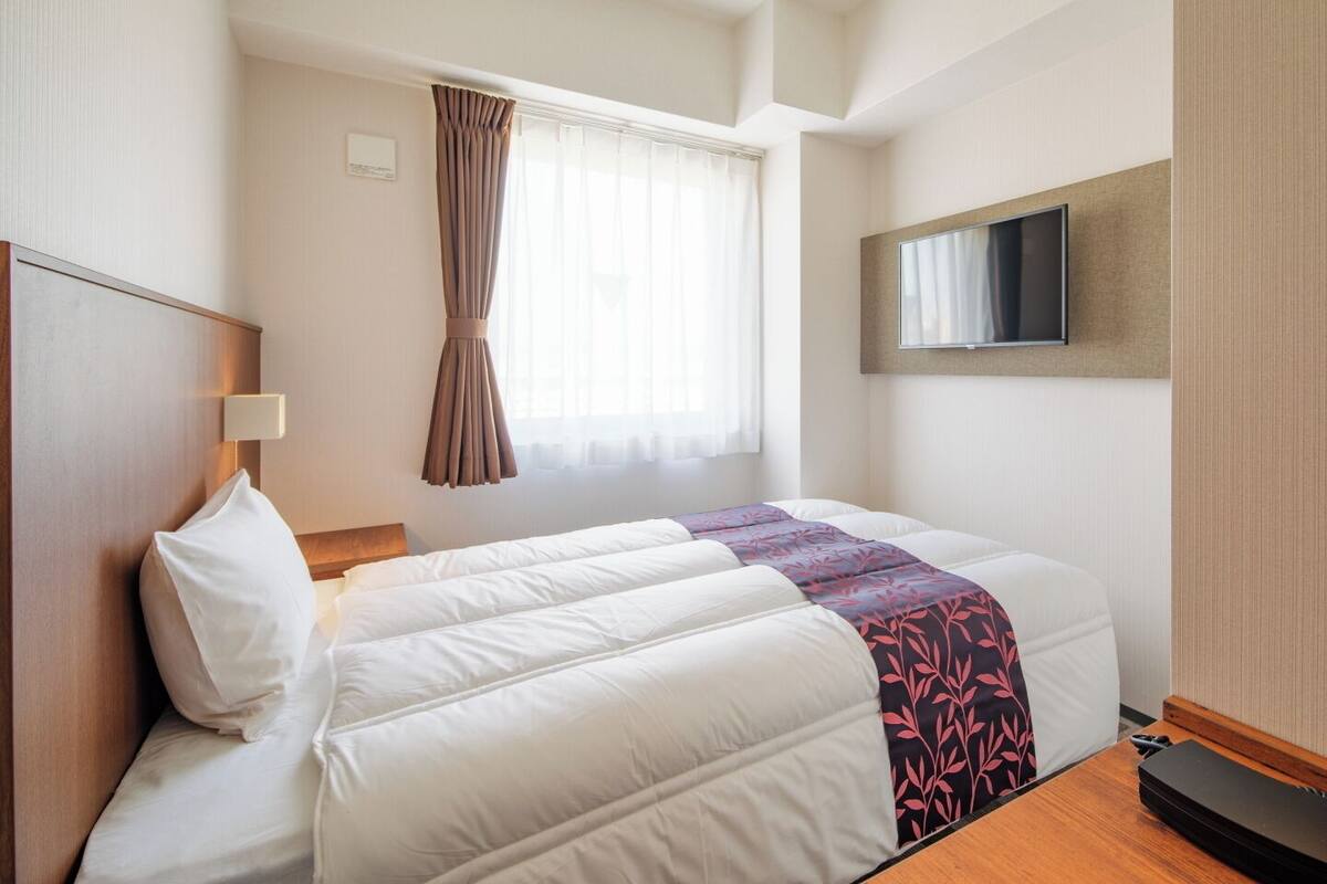 A hotel room with a bed, a TV mounted on the wall, and a window with curtains.