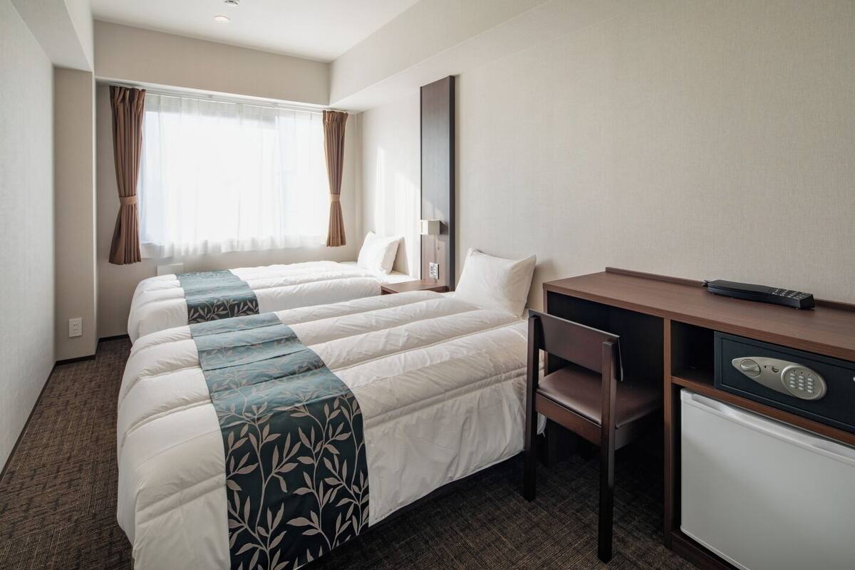 A hotel room with two beds, a desk, a chair, a desk lamp, and a minibar.