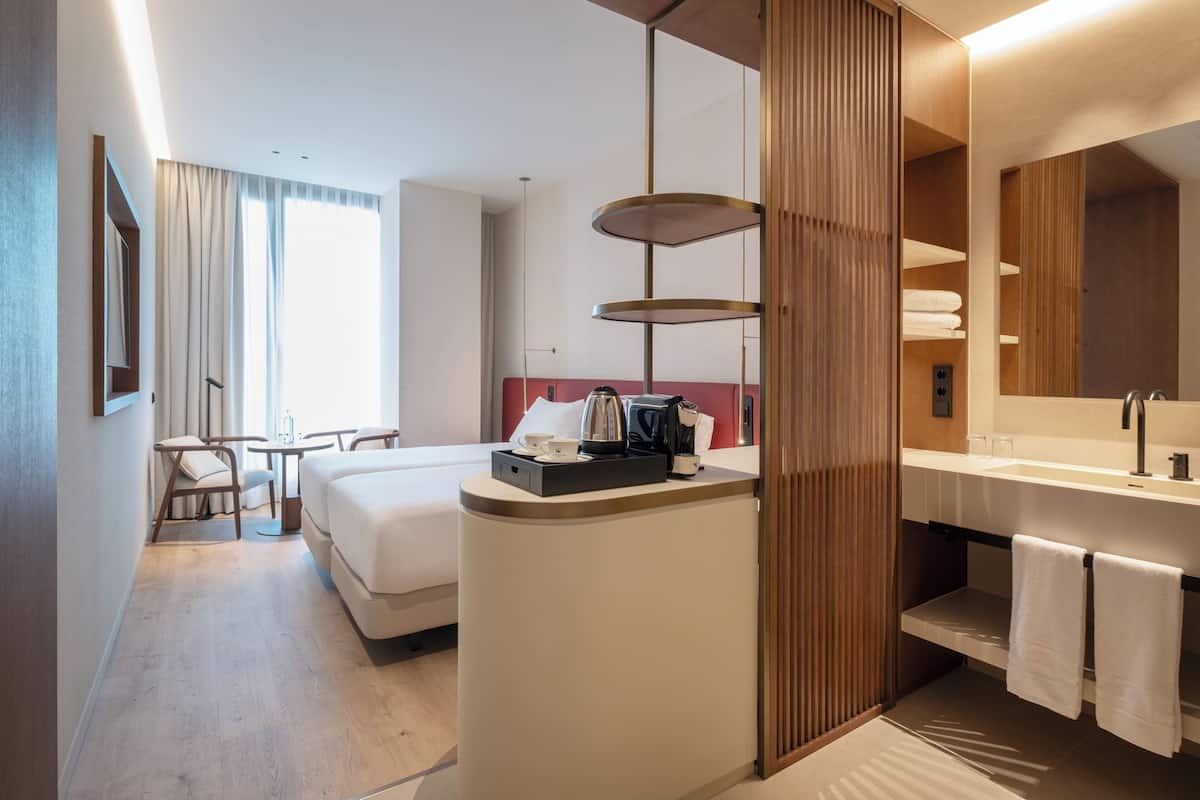 A hotel room with a bed, bedside table, lamp, and a bathroom with a sink and mirror.