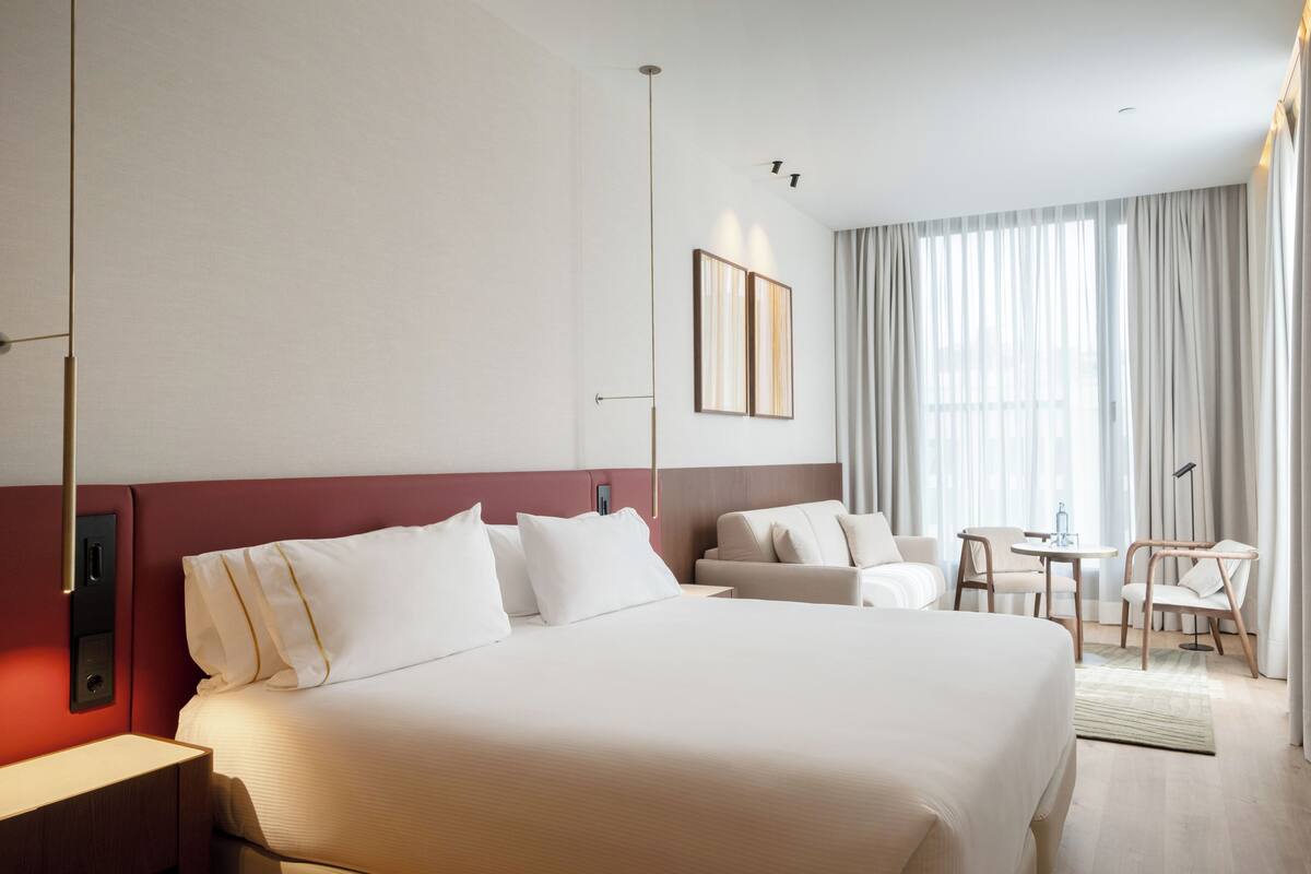 A hotel room with a large bed, a desk, a chair, and a window with curtains.