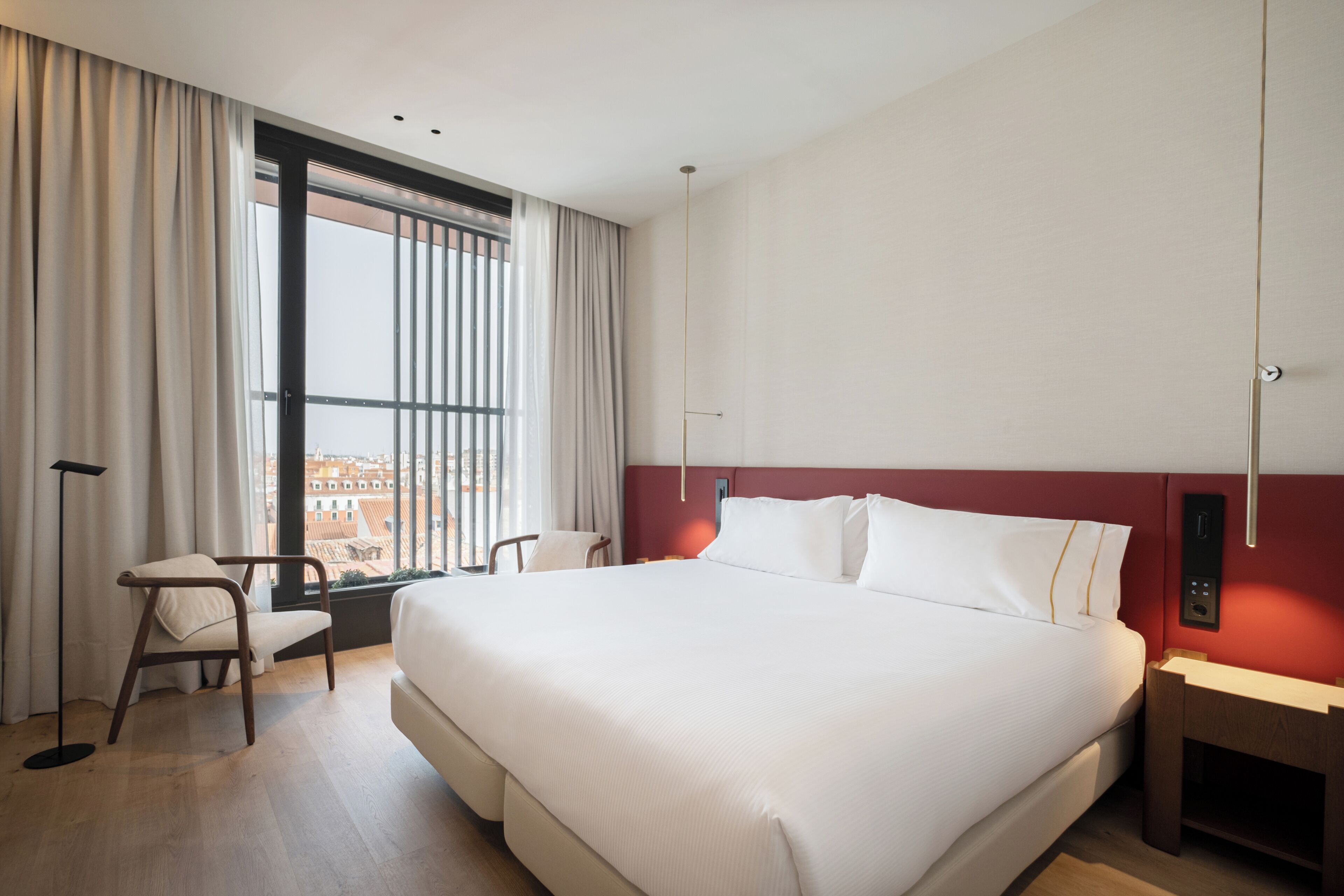A hotel room with a large bed, a desk, a chair, a window with curtains, and a city view.