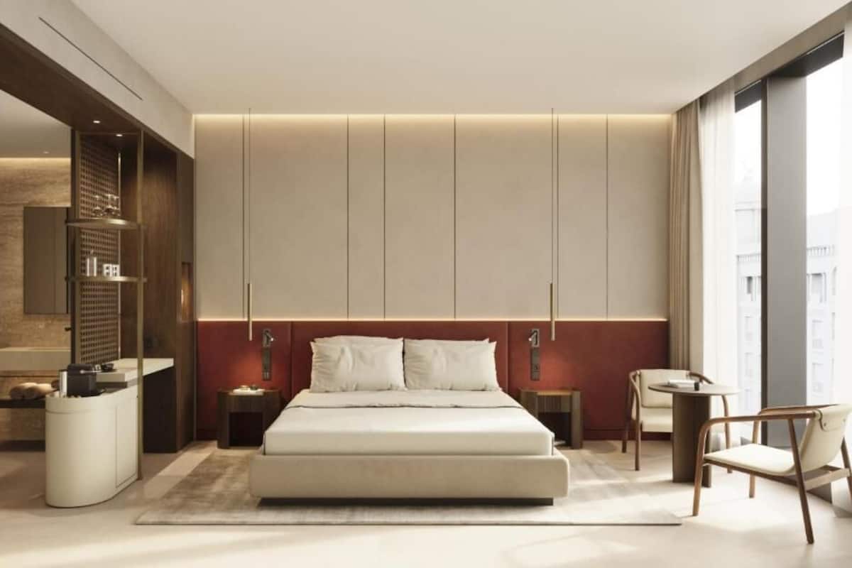 A modern bedroom with a large bed, bedside tables, a built-in wardrobe, and a seating area with a chair and table.