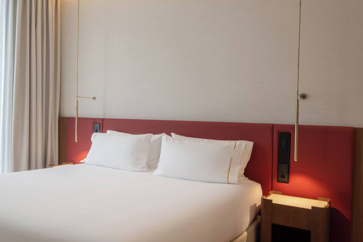 A hotel room with a bed, a nightstand, and a wall-mounted light fixture.