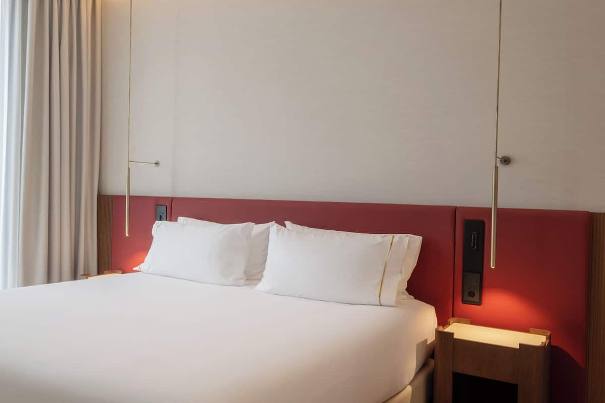A hotel room with a bed, a nightstand, and a wall-mounted light fixture.