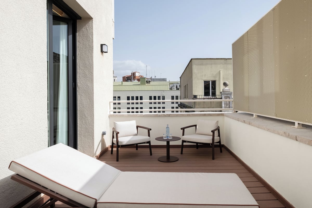 A balcony with a lounge chair, two chairs, a small round table, and a view of buildings in the background.