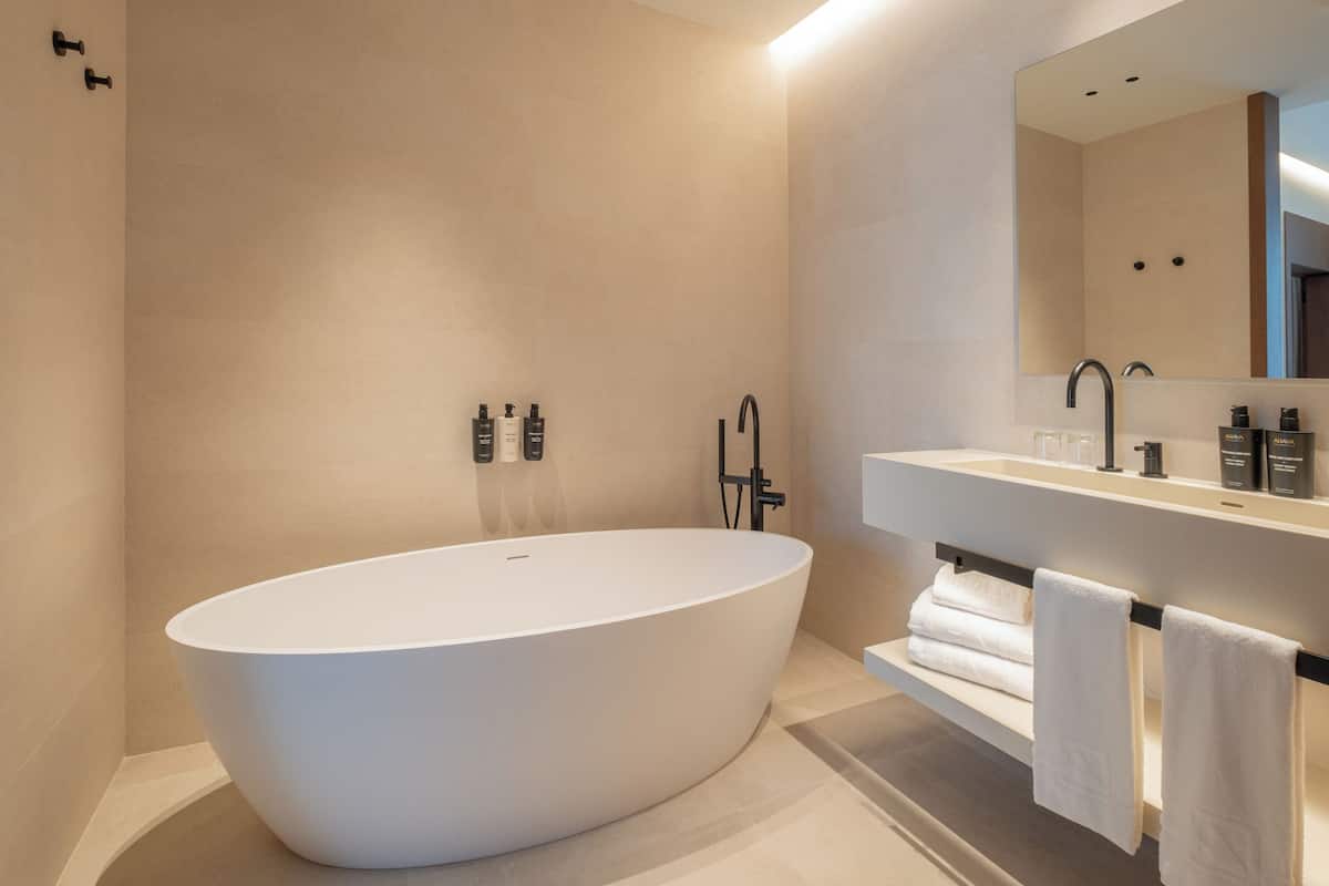 A modern bathroom with a freestanding bathtub, a large mirror, and a vanity with toiletries.