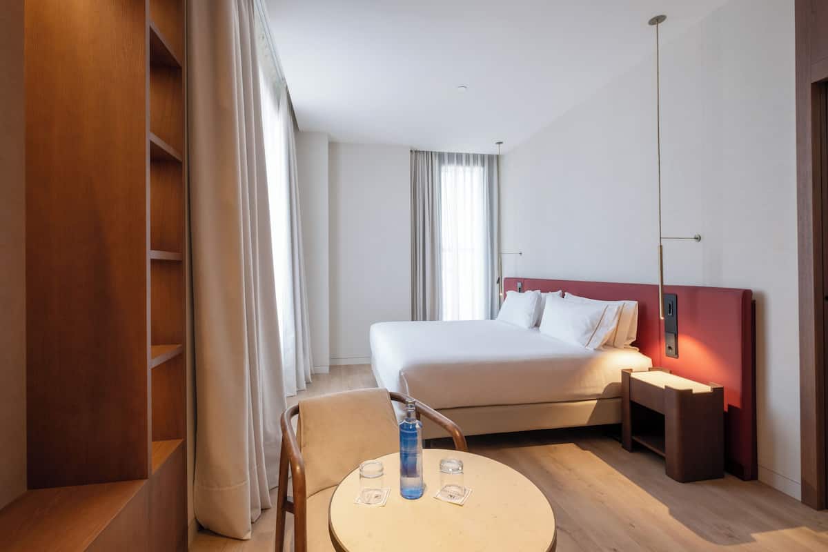 A hotel room with a bed, a round table with two glasses, a bottle, and a chair.