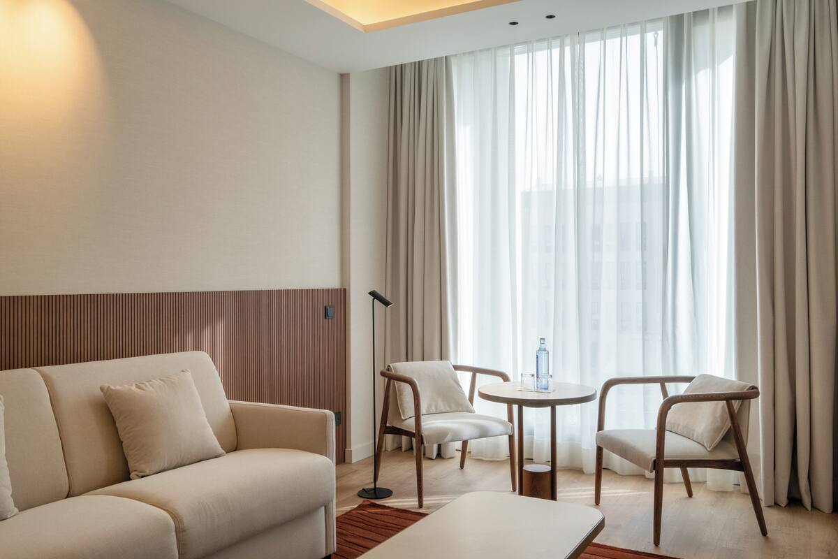 A modern hotel room with a sofa, two armchairs, a small table, and a floor lamp.