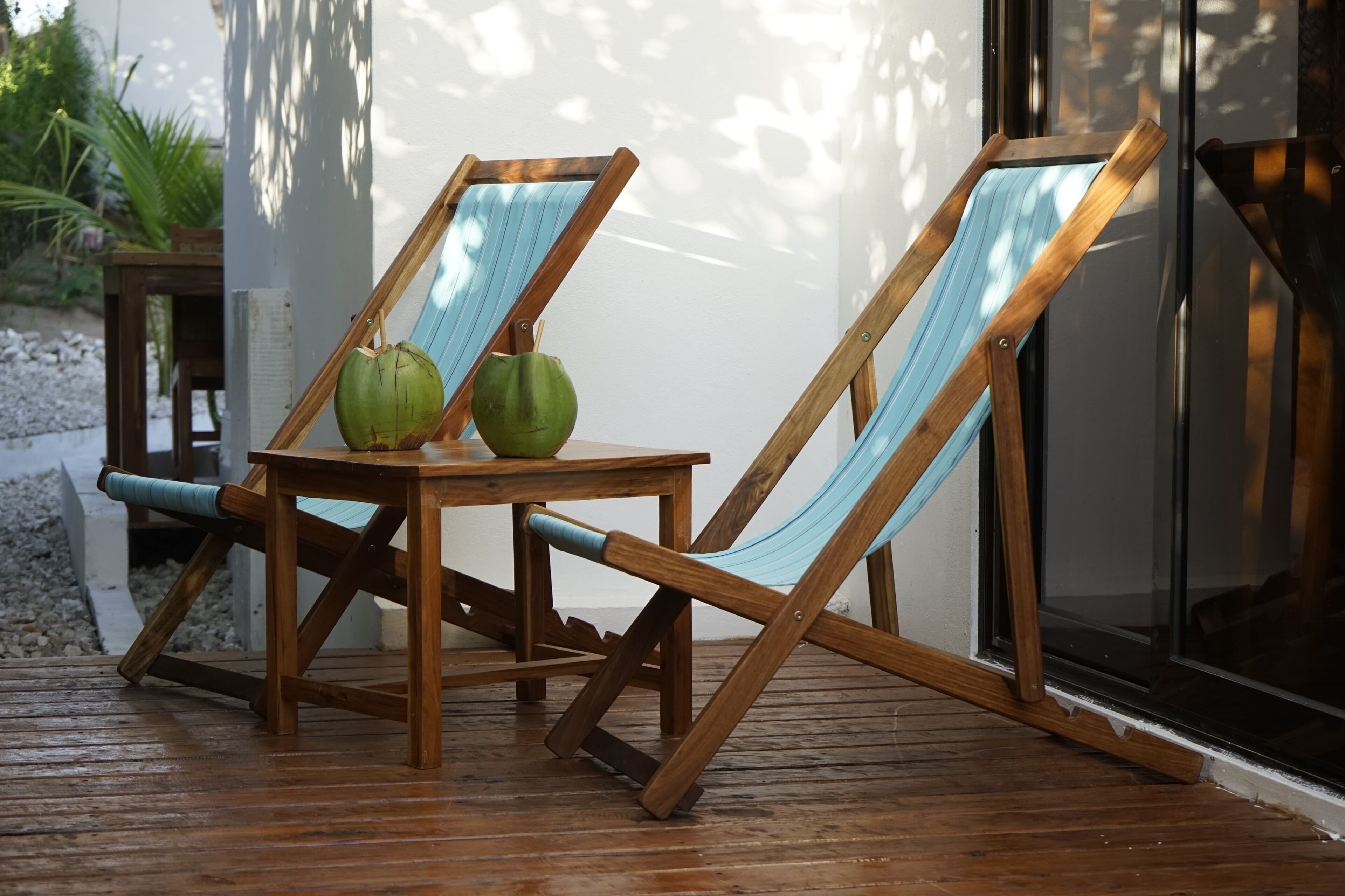 Dos sillones de madera con cojines azules y una mesita de madera con dos cocos verdes.