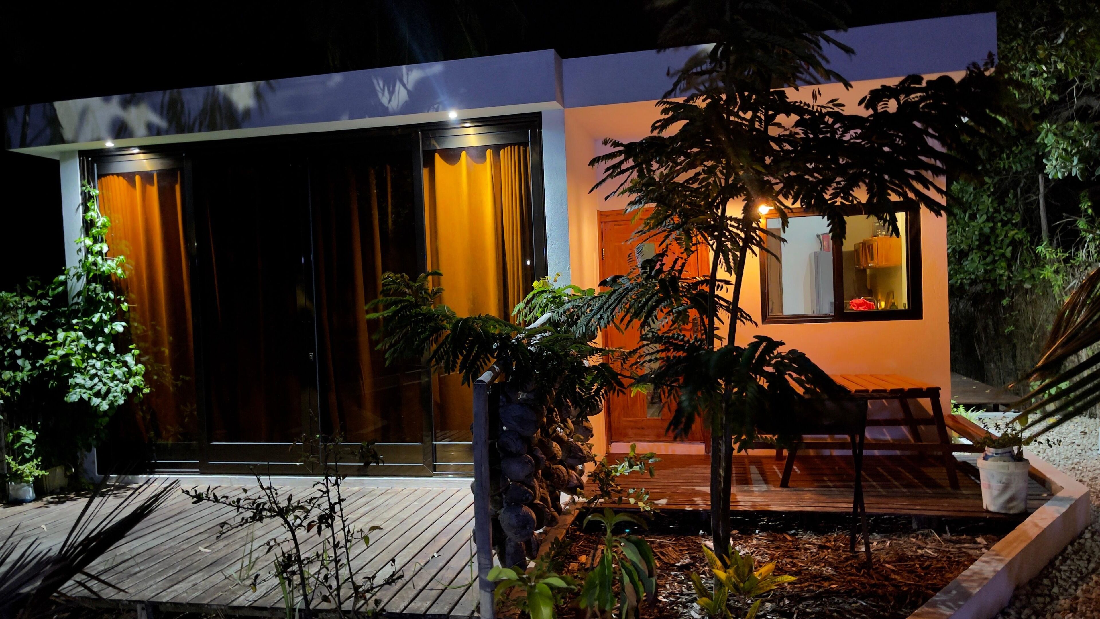 A modern house with a large sliding glass door, a small porch with a bench, and a well-maintained garden.