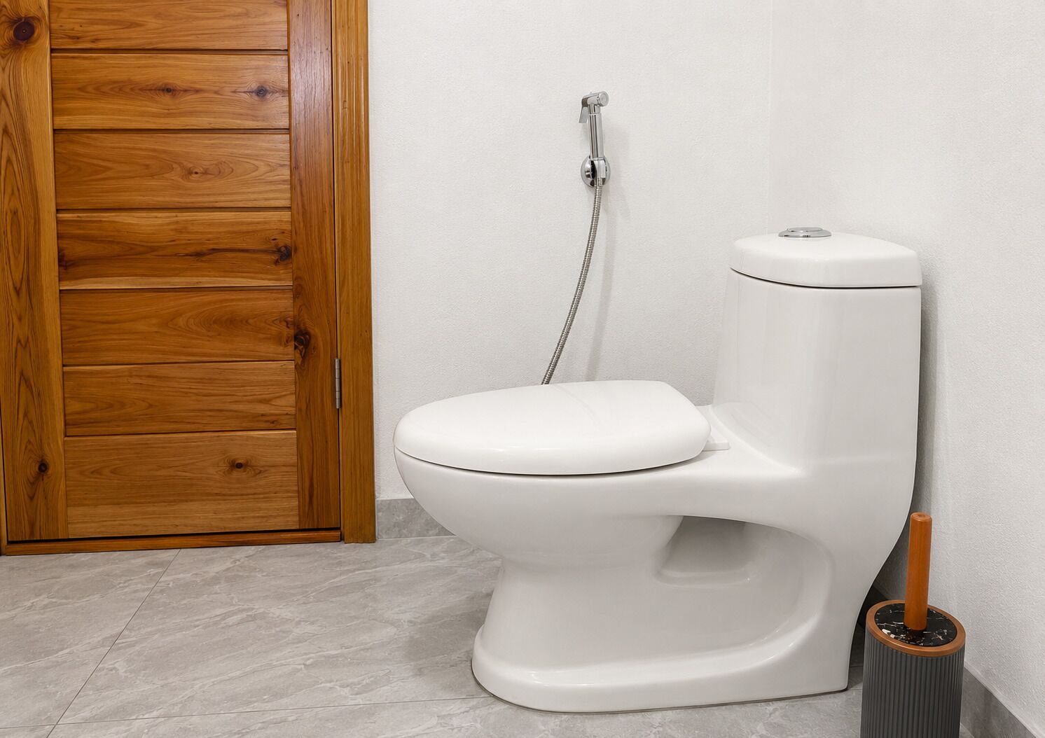 A modern toilet with a shower attachment in a bathroom with a wooden door and tiled floor.