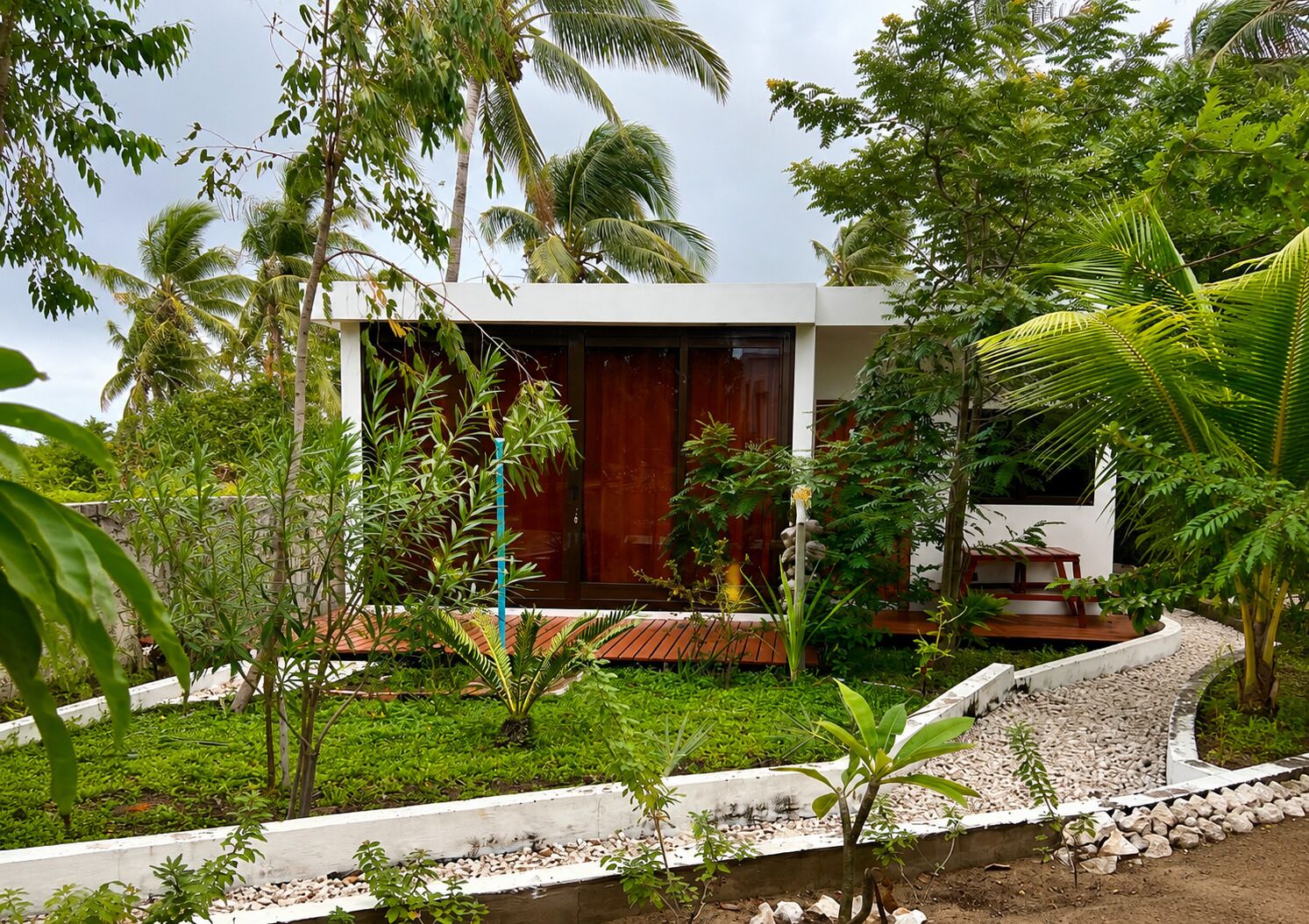 Una casa moderna con terraza de madera, rodeada de vegetación exuberante y palmeras.