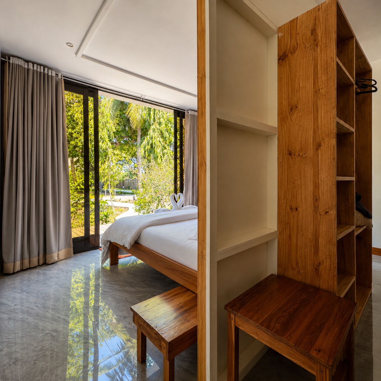 A modern bedroom with a bed, wooden furniture, and a view of greenery outside.