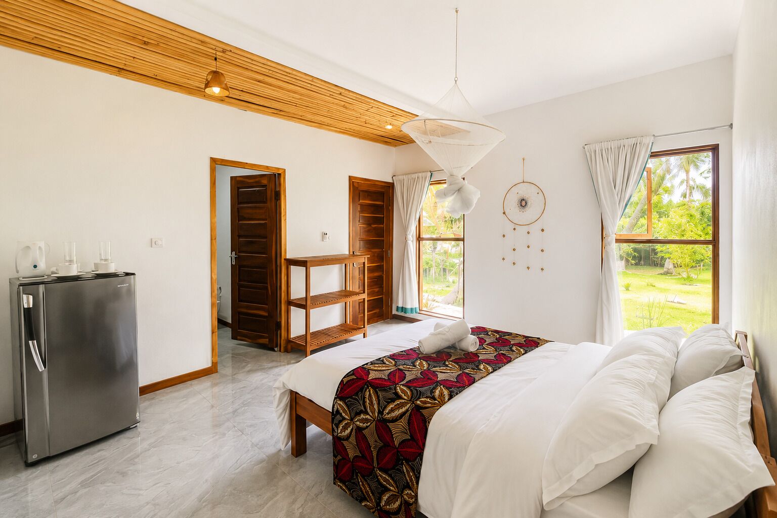 A bedroom with a bed, a wardrobe, a desk, a hanging light, and a view of the outdoors.
