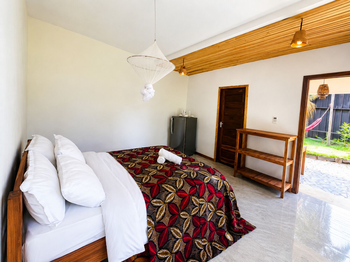 Un dormitorio con cama, un banco de madera, una puerta y una lámpara colgante.