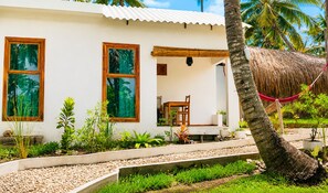 A white building with two windows, a wooden chair, and a thatched roof structure. - cosybe villas Accmmodation (Tofo)