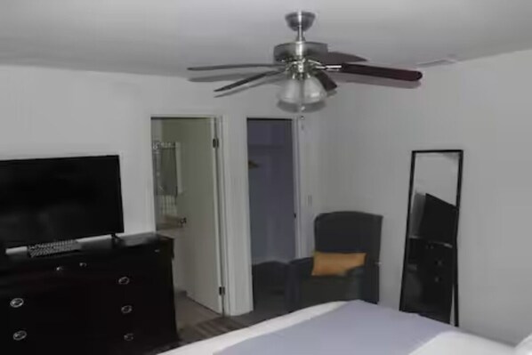 Habitación de hotel con cama, televisor en una cómoda, ventilador de techo y puerta que da a otra habitación.