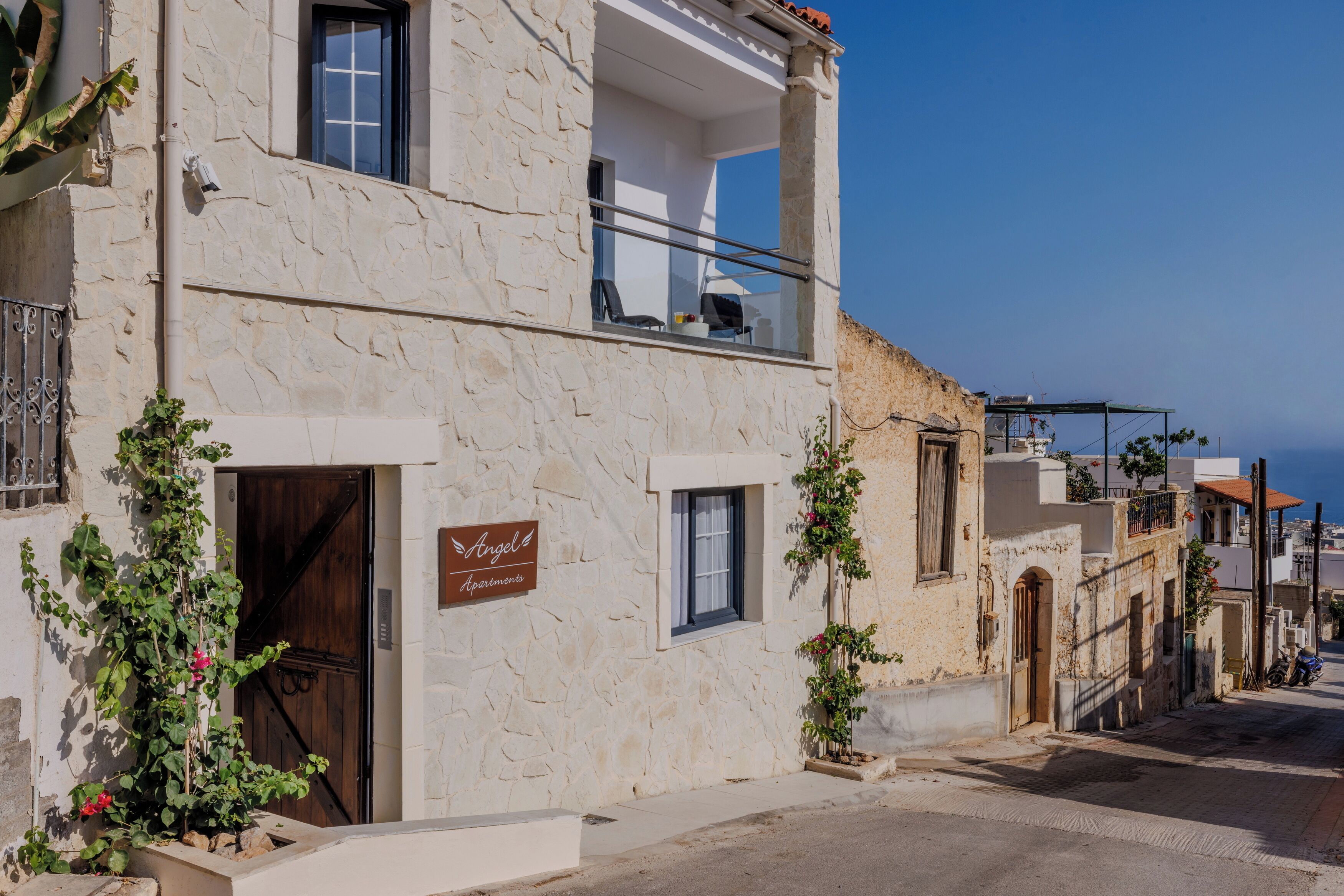 Un immeuble en pierre doté d’un balcon, une enseigne indiquant « Angel Apartments », et une vue sur la rue et la mer.